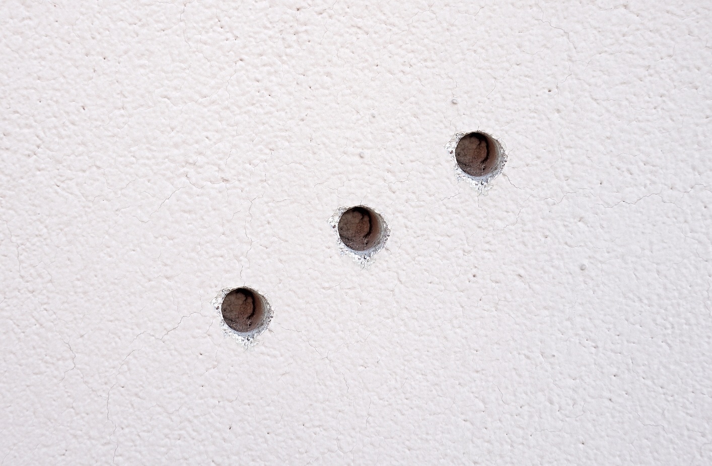 Trzy małe dziury w ścianie po wyjęciu kołków lub gwoździ – powierzchnia do wypełnienia